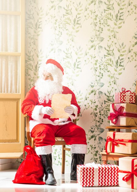 Senior hombre en traje de Santa Claus sentado con lista de deseos
