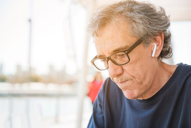 Senior hombre usando anteojos con auricular bluetooth blanco en su oreja