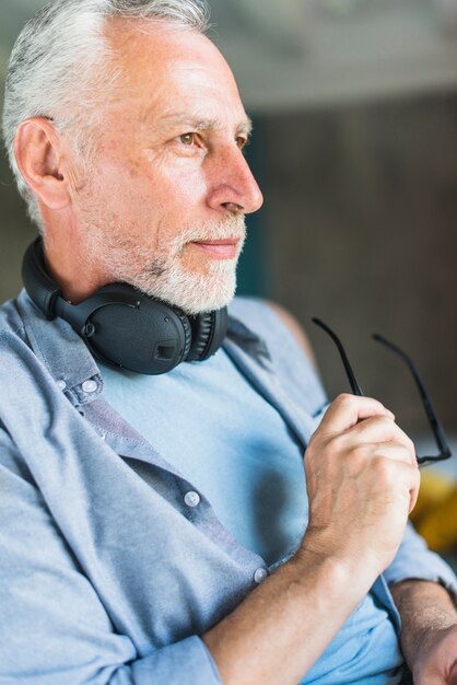 Senior masculino con auriculares alrededor de su cuello sosteniendo anteojos