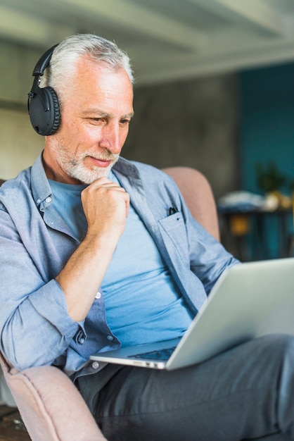 Senior masculino con auriculares negros mirando portátil