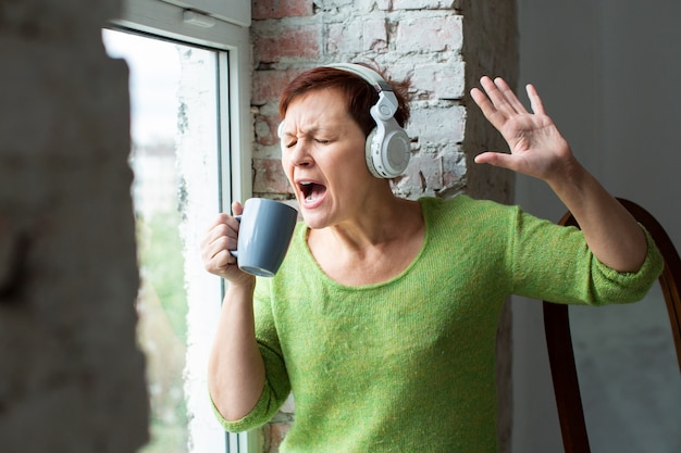 Senior mujer cantando en la taza de café