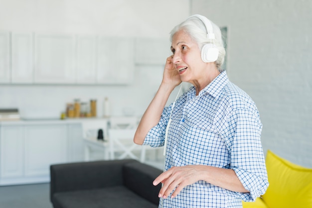 Senior mujer escuchando música en auriculares en casa