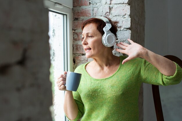 Senior mujer escuchando música y mirando en la ventana