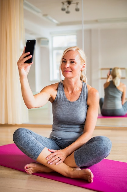 Senior mujer tomando un selfie en estera de yoga