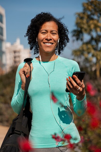 Senior mujer trotando al aire libre con smartphone y auriculares