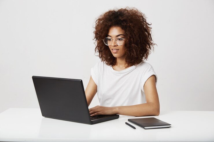 Foto gratuito señora africana del asunto que sonríe trabajando en la computadora portátil sobre la pared blanca.