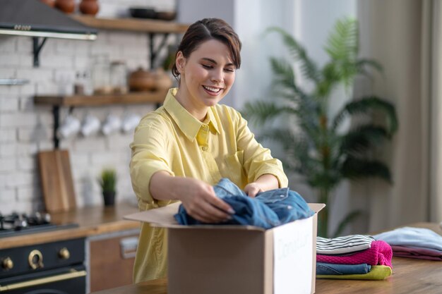 Señora alegre empacando ropa clasificada en una caja de cartón