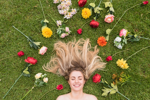 Señora alegre que miente en la hierba entre las flores