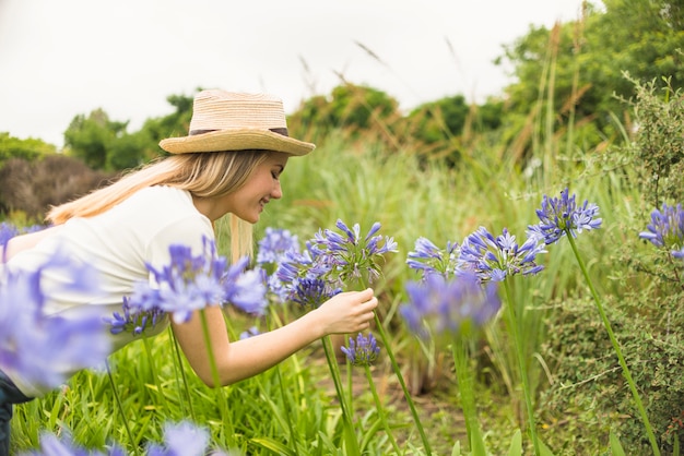 Señora alegre en sombrero cerca de las floraciones azules en parque