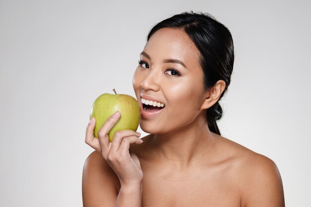 Señora alegre sonriendo y comiendo manzana verde