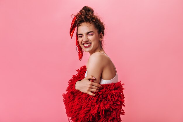 Señora alegre en top blanco y chaqueta roja riendo en rosa