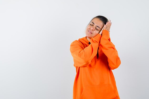 Señora apoyada en las palmas como almohada en sudadera con capucha naranja y mirando pacífica