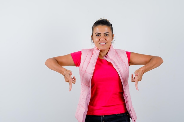 Foto gratuita señora apuntando hacia abajo en camiseta, chaleco y mirando confiada