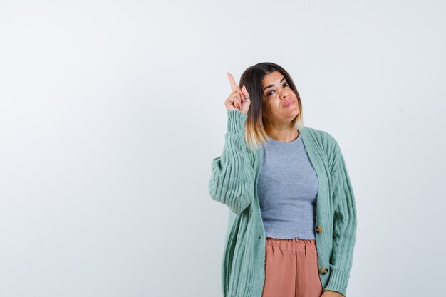 Señora apuntando hacia arriba en ropa casual y luciendo orgullosa, vista frontal.