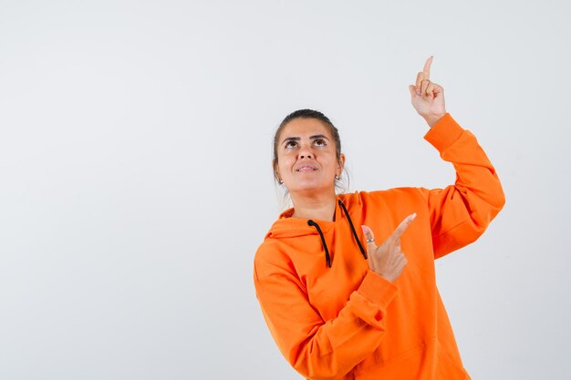 Señora apuntando hacia arriba en sudadera con capucha naranja y mirando feliz