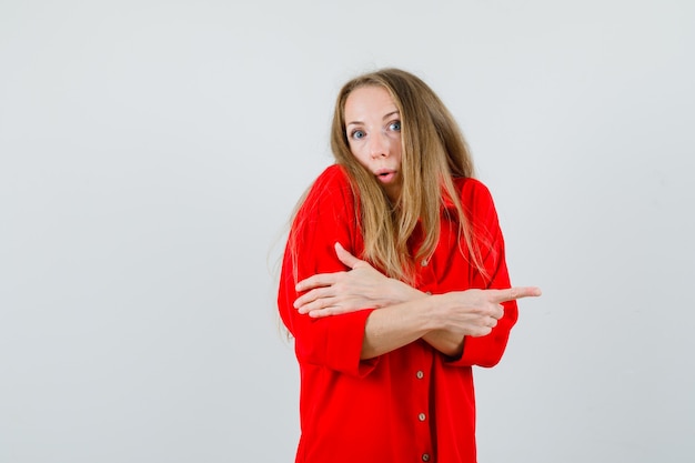 Señora apuntando hacia un lado con camisa roja y mirando confundida,