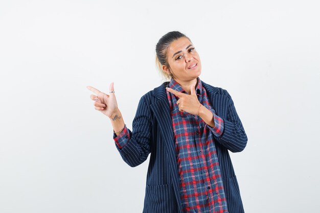 Señora apuntando hacia el lado izquierdo en camisa, chaqueta y luciendo confiada. vista frontal.