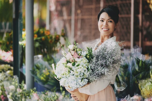 Señora asiática bien vestida posando cerca de la tienda de flores con gran ramo elaborado