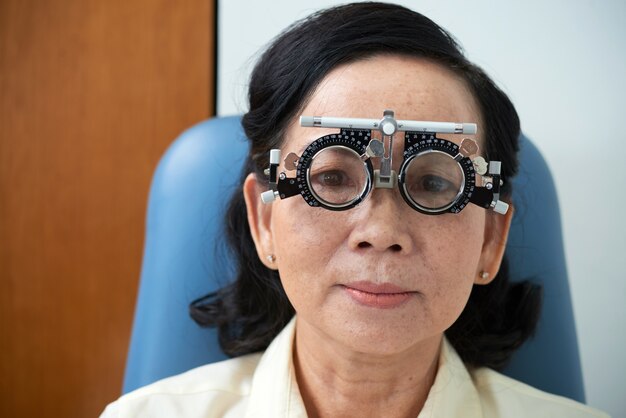 Señora asiática madura con marco de lente de prueba durante el examen de la vista