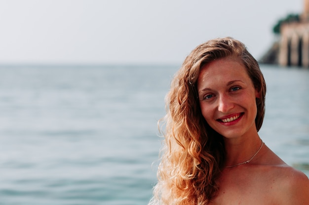 Señora atractiva en bikini bandeau de pie y sonriendo en el mar durante el día.