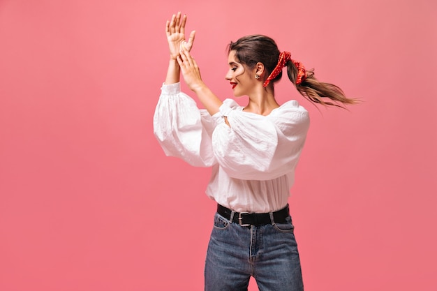 Señora atractiva en blusa blanca aplaudiendo sobre fondo rosa. Bella dama con una venda roja en el pelo y con lápiz labial brillante en poses de blusa.