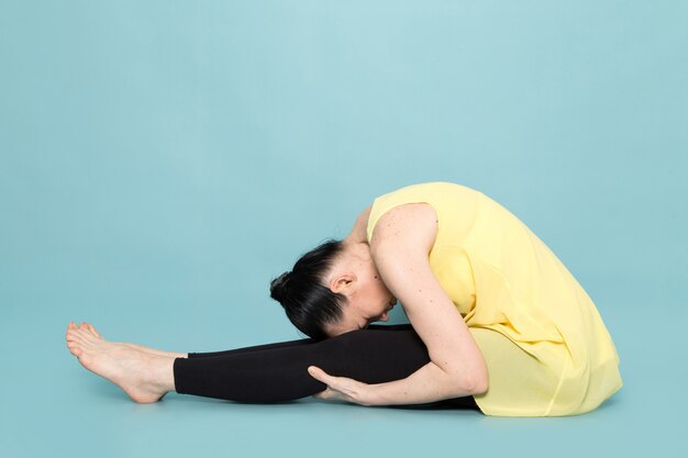 Señora atractiva joven en camisa amarilla y pantalón negro haciendo posturas de yoga