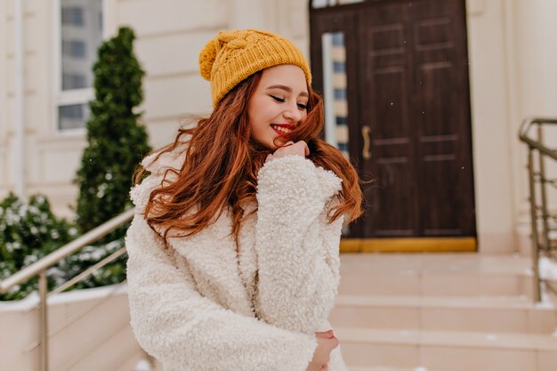 Señora bastante europea en abrigo de invierno que presenta con sonrisa encantadora. Dichosa chica de jengibre expresando emociones positivas.