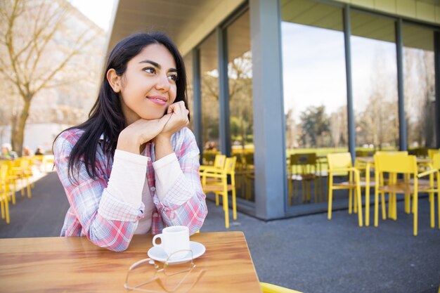 Señora bastante joven positiva que goza bebiendo el café en café