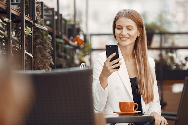 Señora bebe un café. Mujer sentada a la mesa. Chica usa un teléfono.