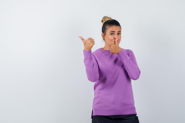 Señora en blusa de lana mostrando gesto de silencio con el pulgar hacia arriba y mirando confiado