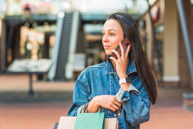 Señora con bolsas y teléfono inteligente en el centro comercial