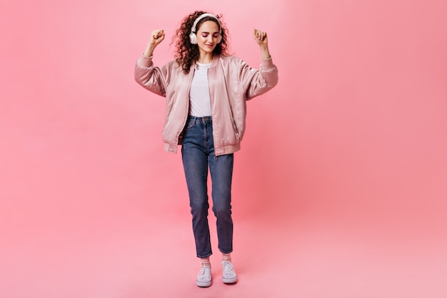 Señora bonita en bailes de auriculares blancos sobre fondo rosa