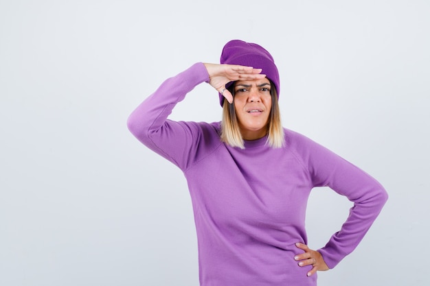 Señora bonita con las manos sobre la cabeza en suéter, gorro y mirando confundido, vista frontal.