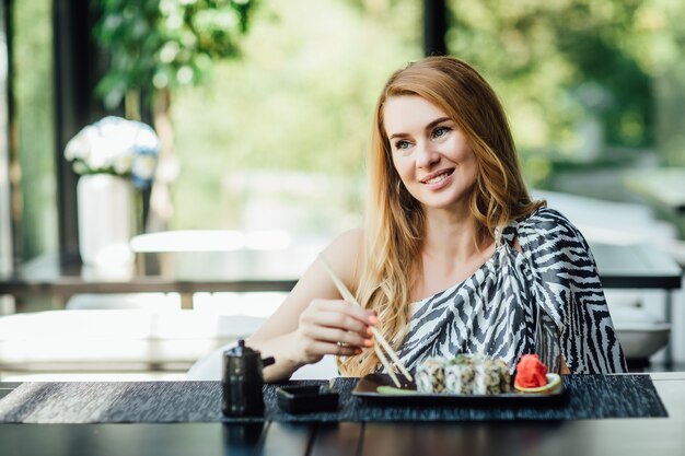 Señora bonita de mediana edad sentarse en el café en la terraza de verano con rollos de sushi