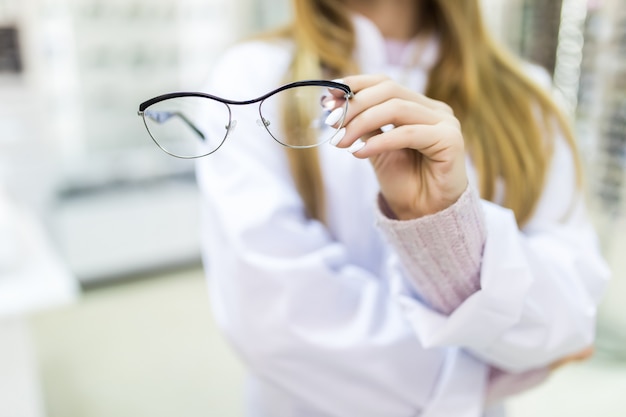 Foto gratuita señora con cabello dorado vestida con un suéter blanco sostiene anteojos médicos en su brazo y mira a través de ellos en una tienda especial