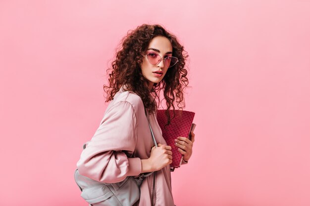 Señora con cabello ondulado mira a cámara y sosteniendo libros