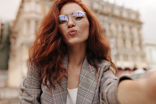 Señora con cabello ondulado sopla beso y toma selfie afuera