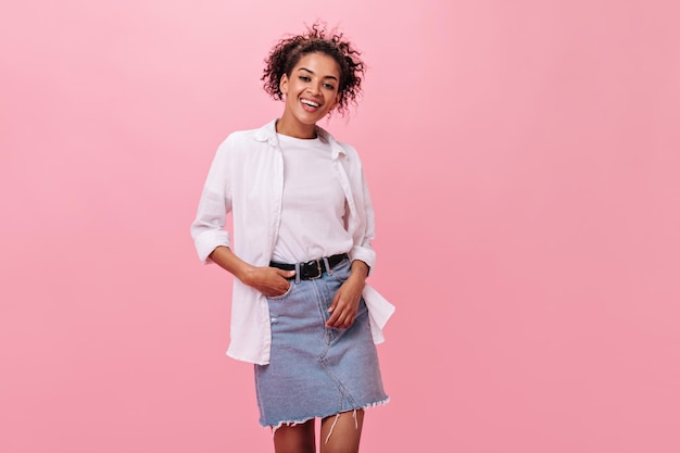 Señora en camisa blanca y falda de mezclilla posando sobre fondo rosa Mujer sonriente en traje elegante mirando a la cámara sobre fondo aislado