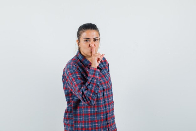 Señora en camisa casual mostrando gesto de silencio y mirando sensible, vista frontal.