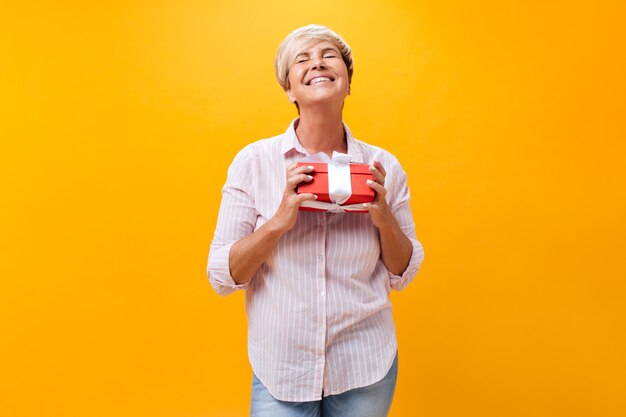 Señora en camisa rosa tiene caja de regalo roja sobre fondo naranja