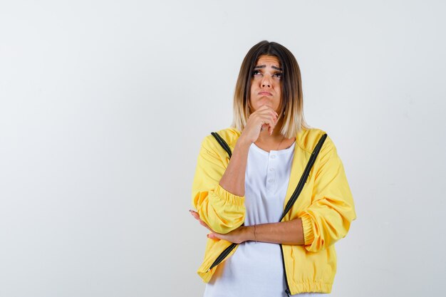 Señora en camiseta, chaqueta apoyando la barbilla en la mano y mirando pensativa, vista frontal.