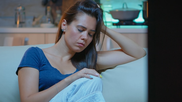 Señora caucásica dormida en el sofá sola en la sala de estar mientras ve la película en la televisión tarde en casa por la noche. Ama de casa solitaria cansada en pijama para quedarse dormido frente a la televisión sentado en un cómodo sofá.