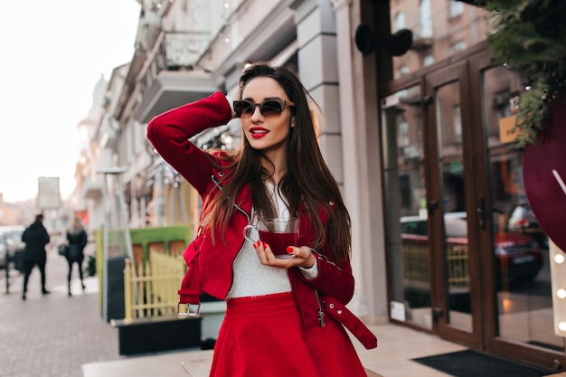 Señora caucásica interesada en gafas negras posando con taza de té