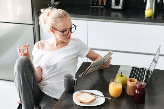 Señora centrada seria leyendo el periódico mientras desayuna