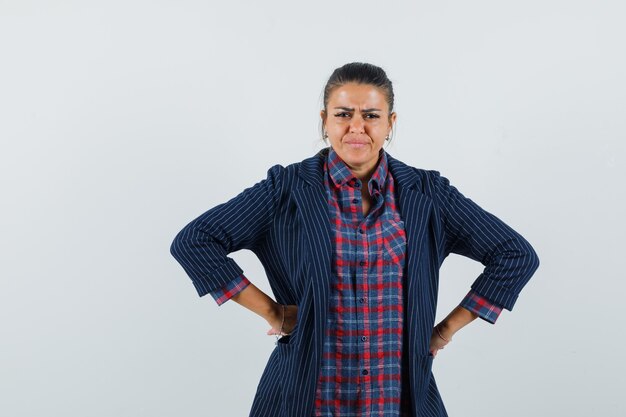 Señora cogidos de la mano en la cintura en camisa, chaqueta y mirando rencoroso, vista frontal.