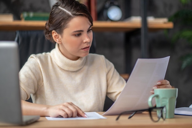 Señora concentrada que examina la documentación en el escritorio