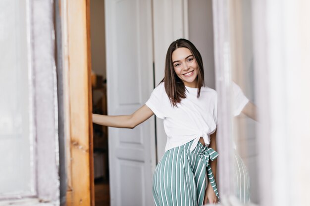 Señora dichosa con cabello castaño sonriendo mientras posa en casa. Foto interior de mujer refinada con peinado de moda.