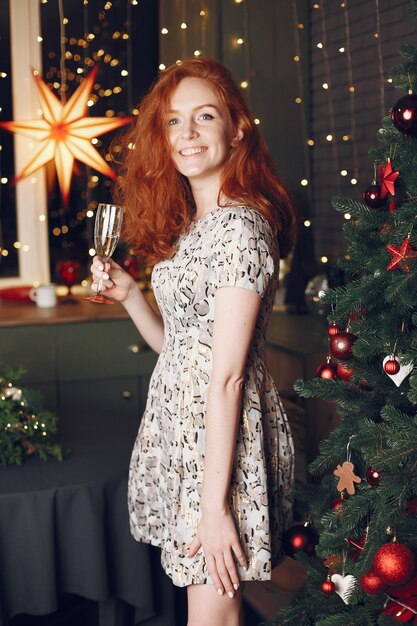 Señora elegante cerca del árbol de Navidad. Mujer en casa con champagne.