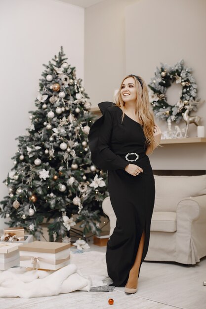 Señora elegante cerca del árbol de Navidad. Mujer en una habitación. Famale con un elegante vestido negro.
