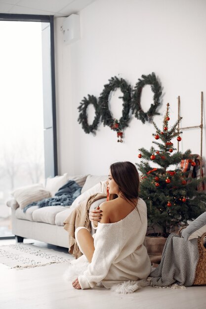 Señora elegante cerca del árbol de Navidad. Mujer en una habitación. Famale con un suéter de punto blanco.